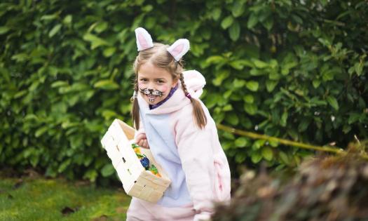 A girl dresses as the Easter bunny and holds a basket filled with colorful eggs.