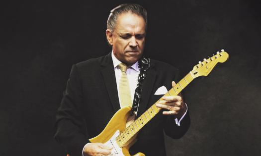 Jimmie Vaughan playing guitar on a black stage