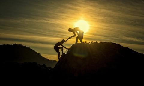 Two men free climb a mountain together in front of the rising sun
