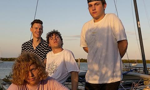 Members of King Peach pose on a sailboat while several boats pass by in the background