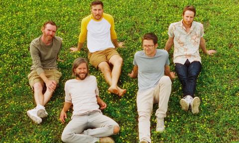 Members of the band Moon Taxi wear neutral colors and pose on lush green grass