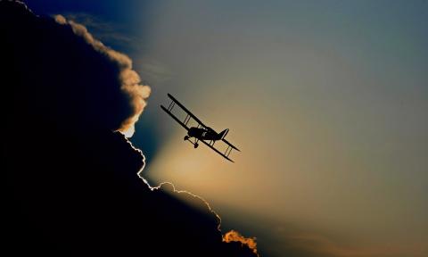 A biplane flying in a sunset sky towards a large cloud whose edges are lined with golden light