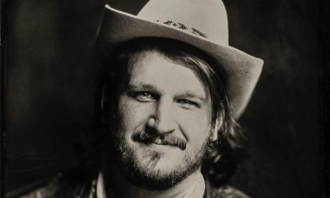 Willi Carlisle, musician, wearing a white cowboy hat against a black background