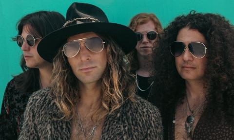 Members from the band Dirty Honey wear glasses and pose in front of a turquoise background.