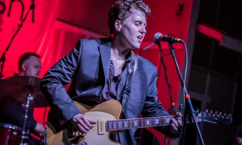 Gabe Stillman sings on a stage with a red backdrop. 