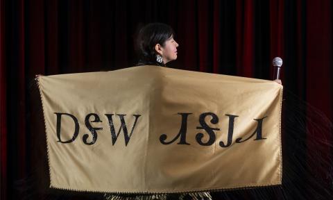 Artist and composer Elisa Harkins on stage with a gold-colored shawl with Native-American words