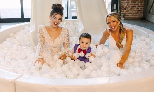 Two brides and a ring boy playing in a wedding-themed ball pit
