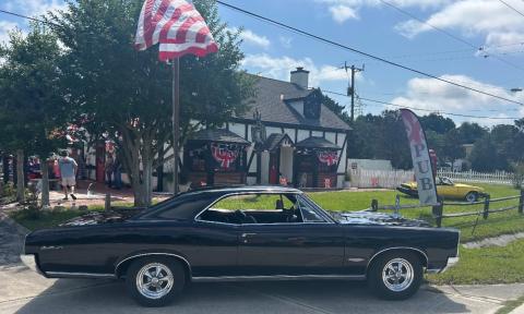 A sleek black antique car parked in front of the Kings Head British Pub, on a breezy and sunny day
