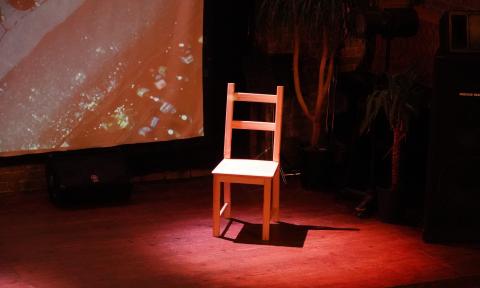 A school chair standing along on stage with a redish spotlight