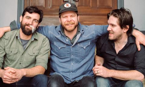 Bandmates from The Last Revel smile and pose while sitting on a staircase. 