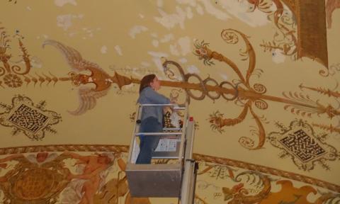 A woman stands in an interior construction lift, while restoring gilded-age decor at Flagler College