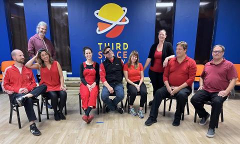 Improv students posing in front of the Third Space Improv logo