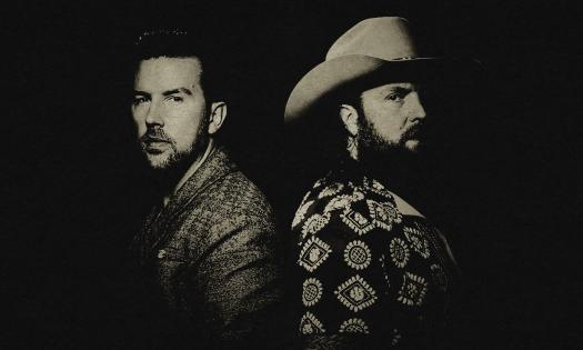 The Brothers Osborne standing back-to-back against a dark background