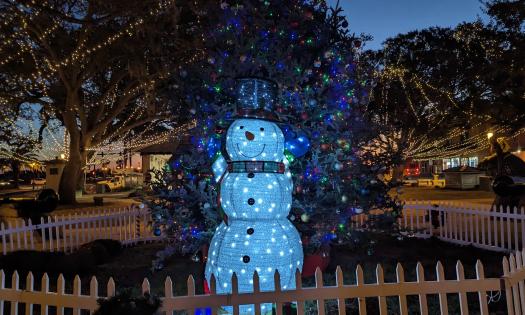 A life-sized snowman, bedazzeled with lights, stands next to the Christmas Tree in the Plaza