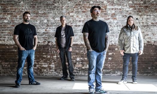 The four-man band, Staind, standing in a warehouse with brick walls