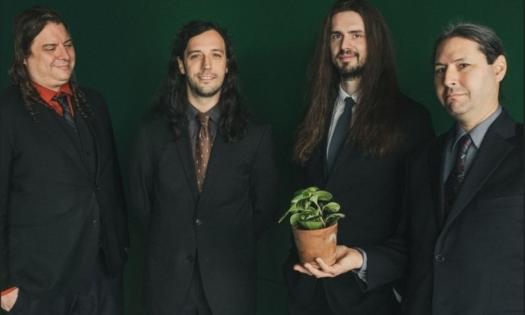 Bandmates from the Henhouse Prowlers smile and pose with a flowerpot in front of a green backdrop. 