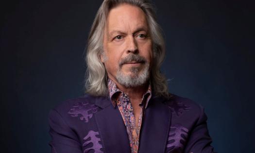Jim Lauderdale poses in a purple blazer in front of a black background.