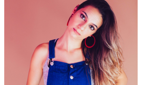 Liz Miele wears a blue jumpsuit and poses with her head canted to the side. 