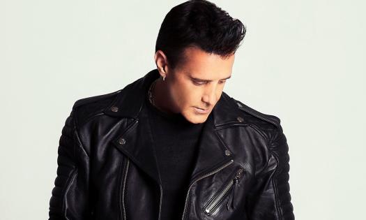 Scott Stapp poses in a leather jacket in front of a white backdrop. 