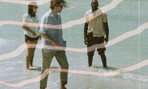 Bandmembers from Surfer Girl pose in clear blue water that rises to their ankles. 
