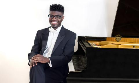 Pianist Kyle Walker, wearing a tux with white tie, seated at a grand piano