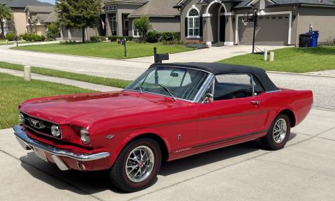 A restored red Mustang in a driveway on a sunny day
