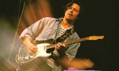 Davy Knowles clutches his guitar and sings to audiences in front of a black backdrop. 