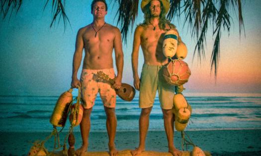 The Wheeland Brothers hold their musical instruments while standing in front of the ocean during sunset.