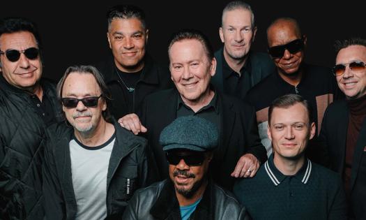 Bandmates from UB40 stand and pose in front of a black backdrop. 