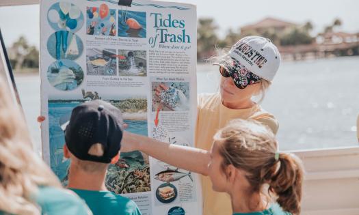 An instructor at Florida Water Warriors points out photos on a poster about trash and wildlife