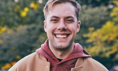 Bo Johnson smiles and poses in brown outwear with a matching shirt. 