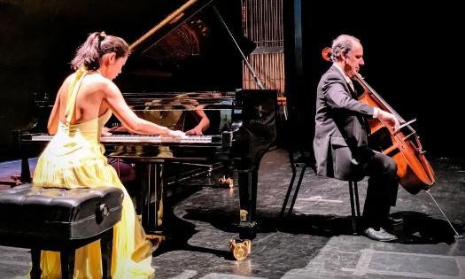 Dr. Catherine Lin, wearing in a yellow gown, plays the piano while Dr. Claudio Jaffe, plays the cello