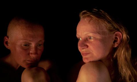 Two women, shown from the neck up, sitting in a dark room