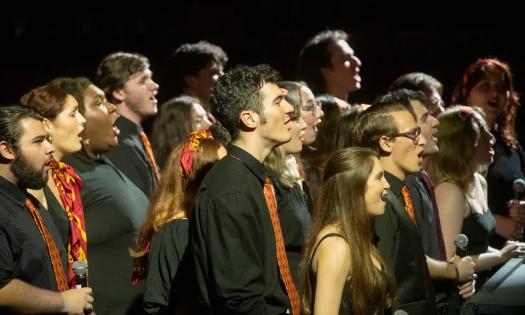 A college a capella choir, in black clothing with red ties and scarfs