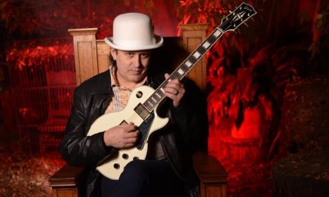Early Times poses with a white hat and matching guitar in front of a red backdrop. 