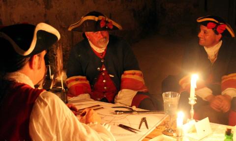 Three reenactors at a table lit by candlelight