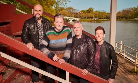 Bandmates from Barenaked Ladies pose on a staircase with a river as a backdrop. 