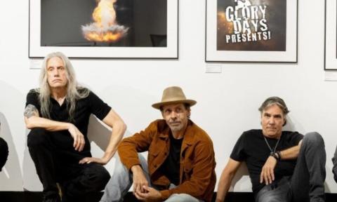 Bandmates from Given To Fly Pose in front of a white wall with framed posters.
