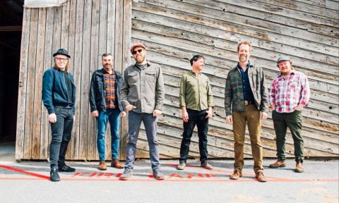Bandmates from Steep Canyon Rangers smile and pose in front of a wooden barn.