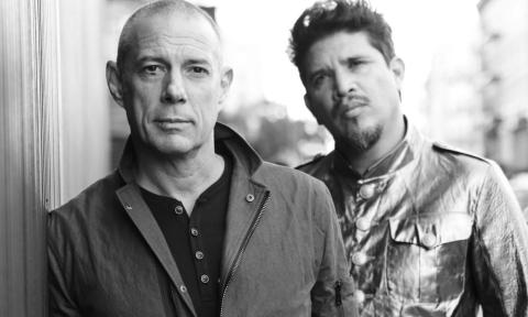 Members of Thievery Corporation stand beside a wall.