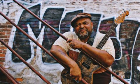 Kevin Burt clutches his guitar on a staircase with graffiti as a backdrop.