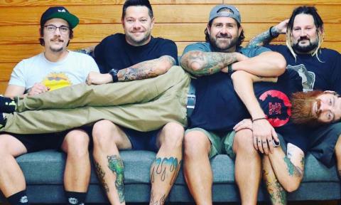 Members of the Supervillains and Kelp strike a pose in front of a rustic wooden backdrop.