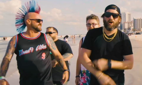Members of Cloud 9 Vibes stroll down a beach as they perform a song together.
