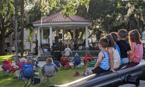 Adults in lawn chairs and children sitting on the cannons, enjoying a concert in the plaza