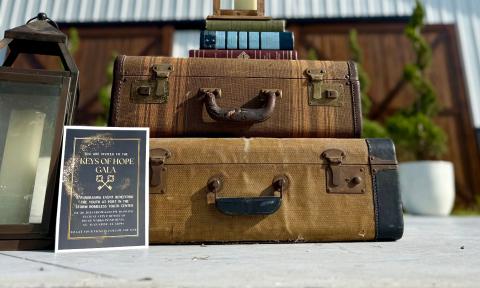 Two old suitcases topped by books promoting a gala for unhoused youth