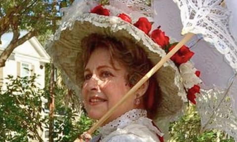 Dianne Jacoby, dressed in white, with a brimmed bonnet and white parasol