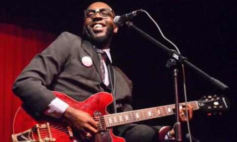 Mr. SIPP smiles and poses with his cherry red guitar.