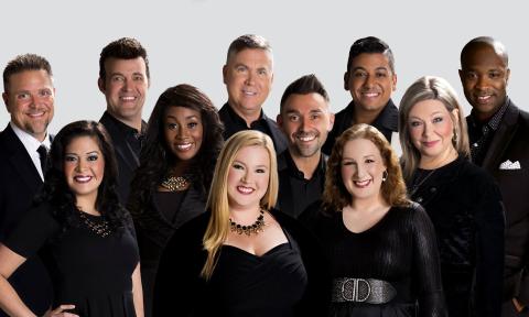 Votave, an 11-member a capella group, wearing black, standing together against a white wall