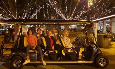 Guests aboard an electric vehicle, sitting by a decorated tree during St. Augustine's Nights of Lights