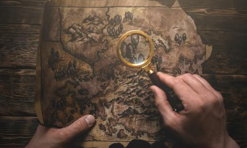 two hands holding an old map, one hand has a magnifying glass